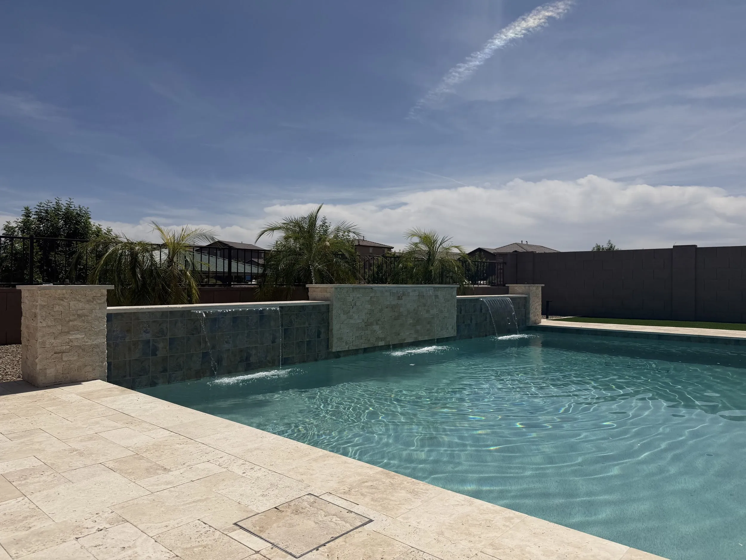 Modern custom pool with travertine deck and stone water wall built by Meraki Pools AZ in Tucson