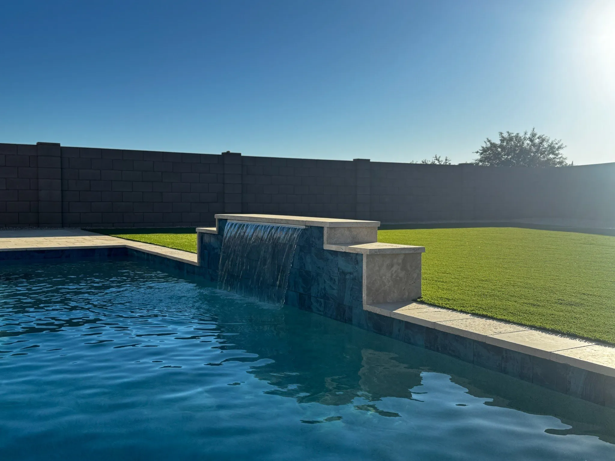 Modern pool with stone water wall and artificial turf